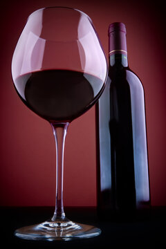 Glass and bottle of red wine, against a red vignetting background.