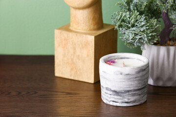 Holder with candle and houseplant on table near green wall in room, closeup