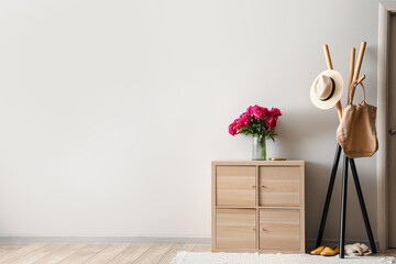 Vase of red peonies with coat rack and dresser near light wall
