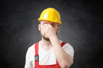 Tired construction worker in yellow hard hat, covering his face