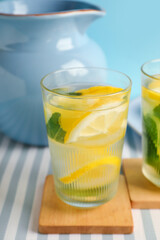 Glasses and jug of infused water with lemon and mint on blue background