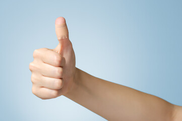 Female thumb with adhesive bandage on blue background