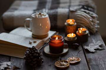 Fototapeta na wymiar Aromatherapy on a grey fall morning, atmosphere of cosiness and relax. Autumn cozy home composition with hot chocolate with marshmallow and candles. Wooden background, books, close up.