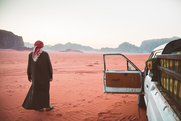 Bedouin driver tour organizer stand in Wadi rum desert by four wheel drive vehicle after sunset....