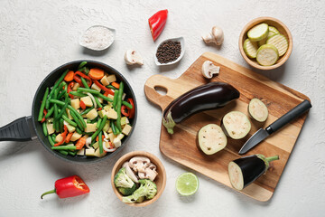 Frying pan and wooden board with fresh vegetables on light background