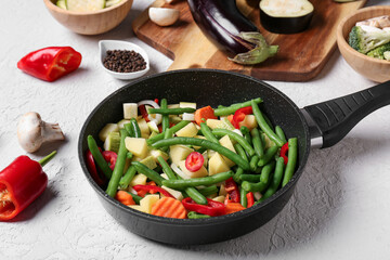 Frying pan with fresh vegetables on light background