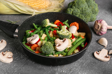 Frying pan with fresh vegetables on grey background