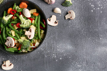 Frying pan with fresh vegetables on grey background