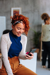 Portrait of young Hispanic woman smiling while using phone during work in office.