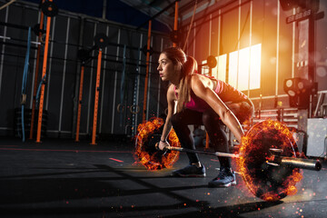 Determined athletic girl works out at the gym with a fiery barbell