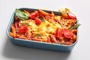 Baking dish of pasta with tomato sauce and cheese on grey background