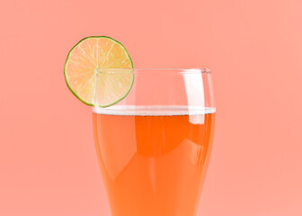 Glass of cold beer with lime on pink background