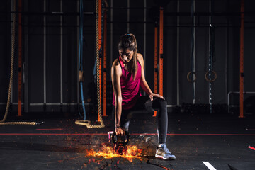 Determined athletic girl works out at the gym with a fiery kettlebell