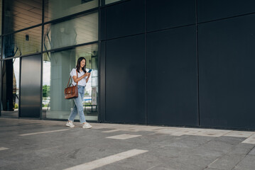 Young busy successful beautiful Japanese business woman, Japanese professional businesswoman holding cellphone using smartphone standing or walking on big city urban street outside