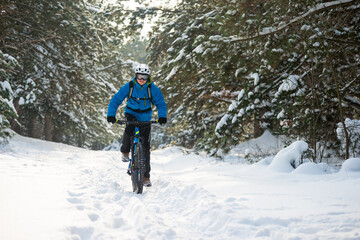 Fototapeta na wymiar Cyclist in Blue Riding the Mountain Bike in the Beautiful Winter Forest Covered with Snow. Extreme Sport and Enduro Biking Concept.
