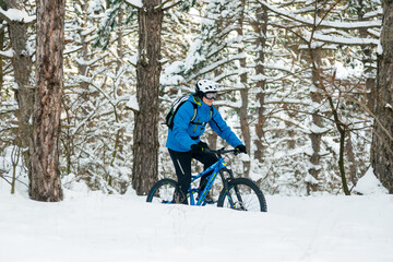 Cyclist in Blue Riding the Mountain Bike in the Beautiful Winter Forest Covered with Snow. Extreme Sport and Enduro Biking Concept.