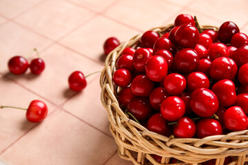 Wicker bowl with sweet cherries on pink tile background