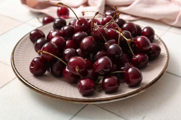 Plate with sweet cherries on white tile table