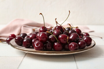 Plate with sweet cherries on white tile table