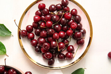 Plate with sweet cherries on light tile background