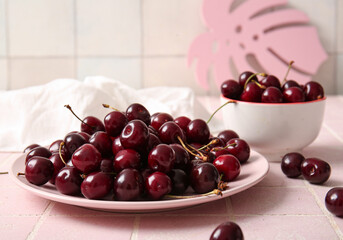Plate and bowl with sweet cherries on pink tile table
