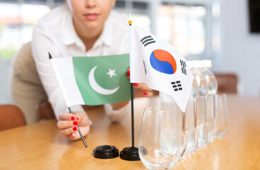 Female employee of the delegation sets flags of countries of South Korea and Pakistan on the table...
