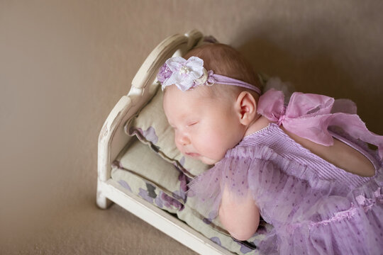 a beautiful little girl in a purple dress sleeps on a small bed. close-up portrait.  newborn baby girl in a beautiful picture