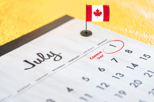 Close-up photograph of a calendar dedicated to the month of July and particularly the date of July 1 surrounded in red marker to celebrate Canada's National Day with a mini desk flag on the background