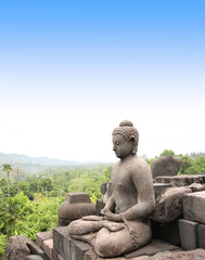 Fototapeta na wymiar Ancient statue of a meditating Buddha in Borobudur Buddhist Temple, Java Island, Indonesia. On blue sky background