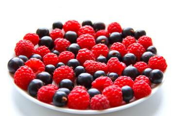 juicy raspberries and blackcurrants on a plate on a white table. selective focus. High quality photo