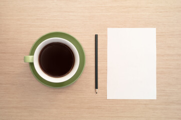 Obraz na płótnie Canvas A green cup of coffee on the background of a table and a white sheet of paper simulates the beginning and pencil