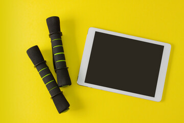 Sport flat lay composition with tablet mockup with blank screen,  black dumbbells on yellow paper background. Top view, horizontal orientation.