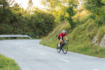 Professional female racing road cyclist riding very fast downhill and at a curve, on a race route along the asphalt forest road