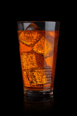 Glass of orange energy carbonated soda drink with ice on black background