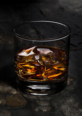 Elegant glass of whiskey with ice cubes on stone background