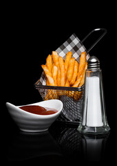 Basket of freshly made southern fries with ketchup and salt black paper on black studio background
