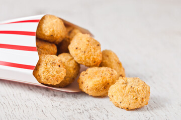 Paper container with fried crispy chicken popcorn nuggets on wooden background