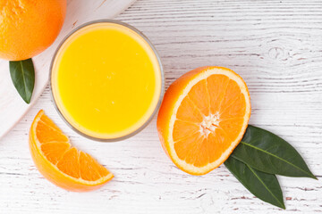 Naklejka na ściany i meble Glass of organic fresh orange smoothie juice with raw oranges on white wooden background.Top view