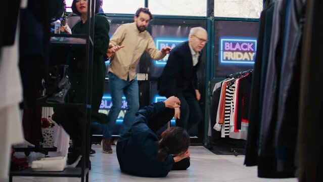 Customer falling in clothing store, getting hurt by crazy anxious crowd of people pushing red tape. Careless shoppers fighting with security guard, black friday madness. Tripod shot.