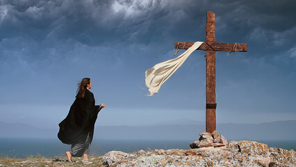 A woman in a black cape approaches the Holy Cross on a stormy day.