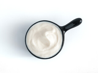 Fototapeta na wymiar Beautiful greek yogurt or sour cream in black bowl, isolated on white background with clipping path. Top view or flat-lay.