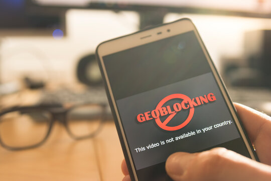 Hands using a smartphone and being unable to navigate online. Geoblocking concept.