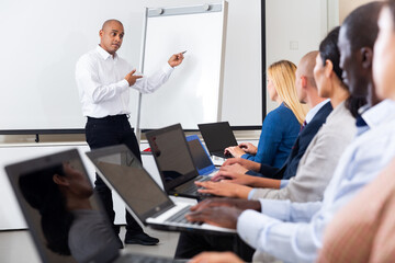 Portrait of hispanic business coach giving talk before participants of corporate training sitting with laptops in meeting room