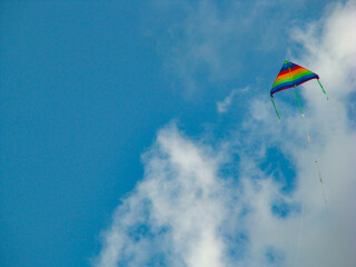 A beautiful and lonely colorful kite in blue, green, yellow, red colors soaring in the air on a beautiful blue sky day with few white clouds