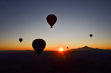 Five balloons flying in the sky contemplating the sun rising behind the mountains, leaving the sky...