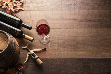 Excellent red wine bottles, wineglass, barrel and corkscrew on a rustic wooden table: traditional...