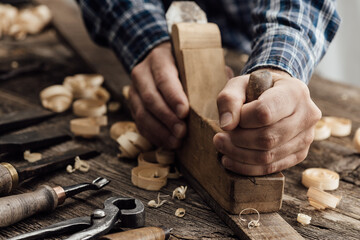 Carpenter working in his workshop, he is smoothing a wooden board using a planer, carpentry,...