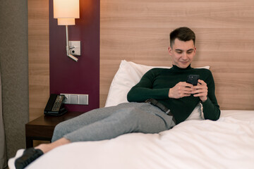 a young guy in the room of a luxury hotel room holds a smartphone in his hands and solves business issues after a trip