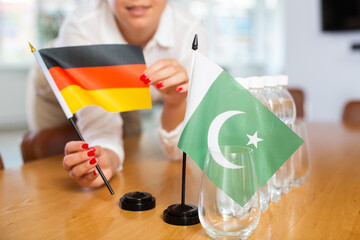 Little flag of Pakistan on table with bottles of water and flag of Germany put next to it by positive young woman 