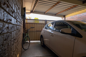 A covered car port with single car storage space and locked metal gate that provide security shelter to a family car and a bike in a suburban home of Australia.